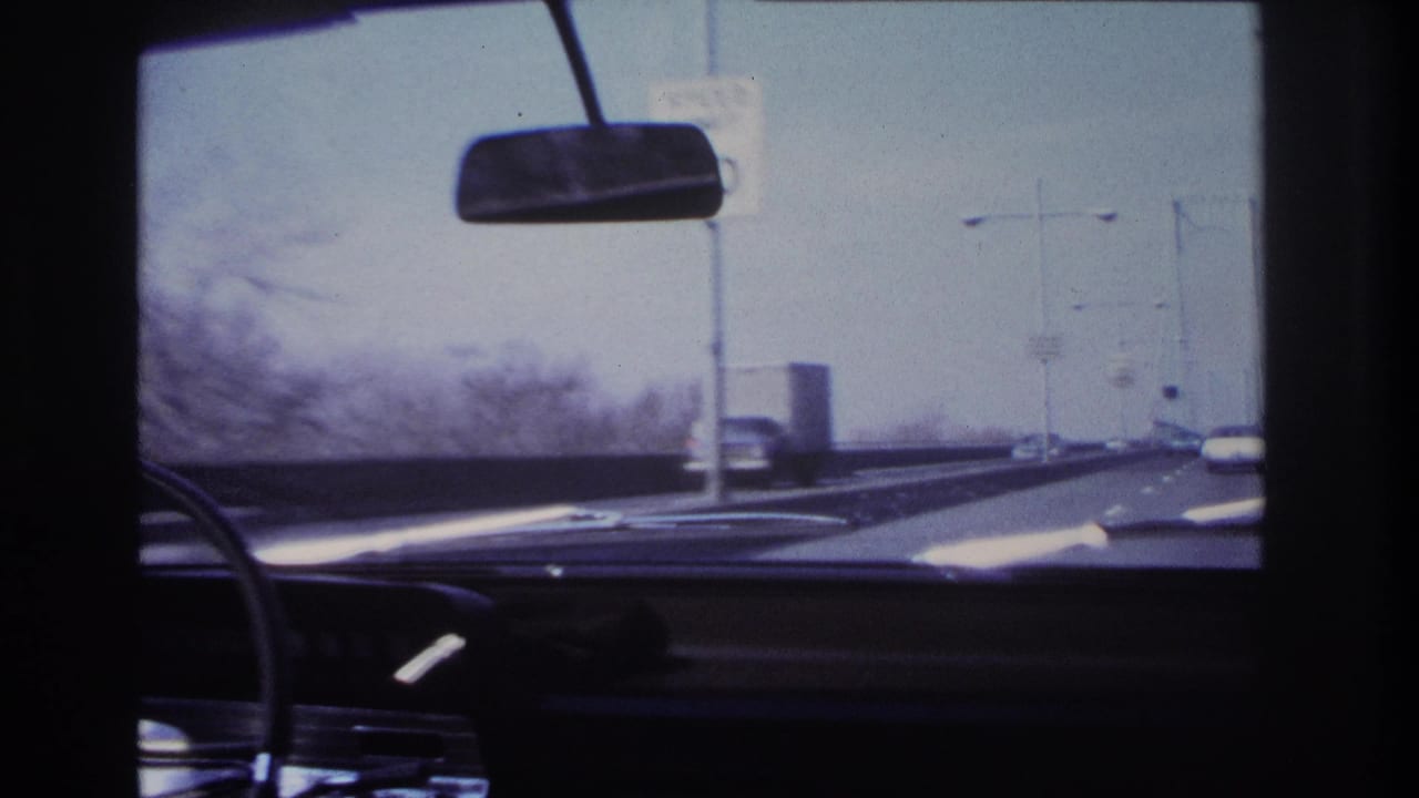 Forward-facing car interior view near Hoboken in 1966, showing the dashboard, windshield, roadside poles and traffic on the road ahead.