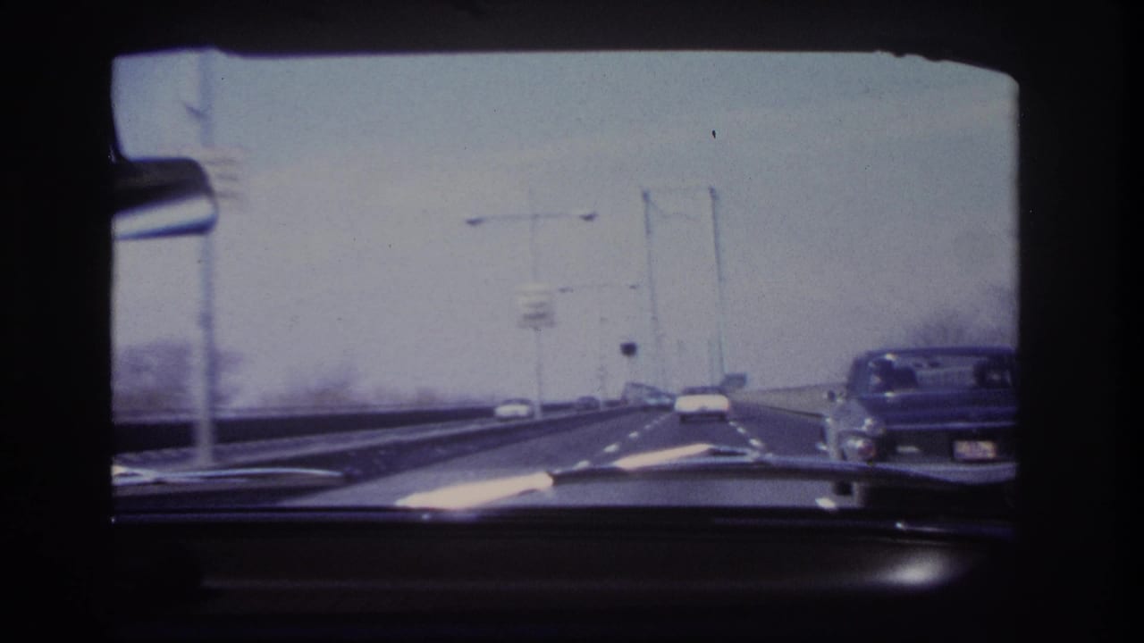1966 in-car bridge footage near Hoboken, with a dashboard foreground, roadway lights, cars ahead, and a classic car visible along the right edge.