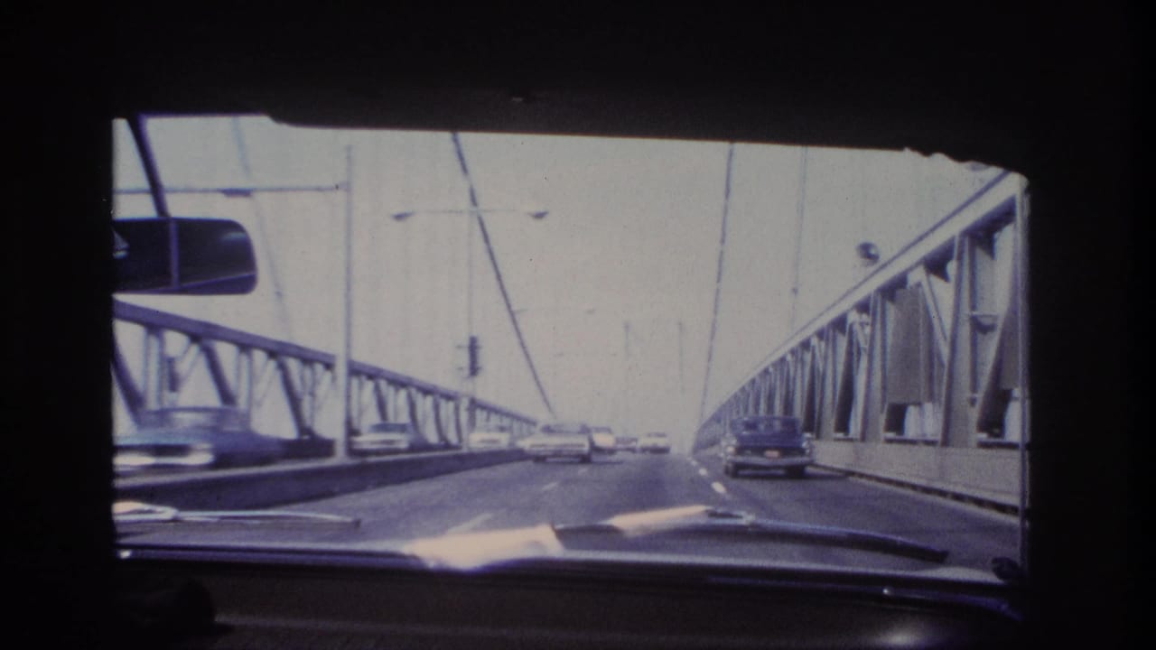 Dashboard-level 8mm frame showing traffic on a suspension bridge in the supplied Hoboken, New Jersey 1966 context.