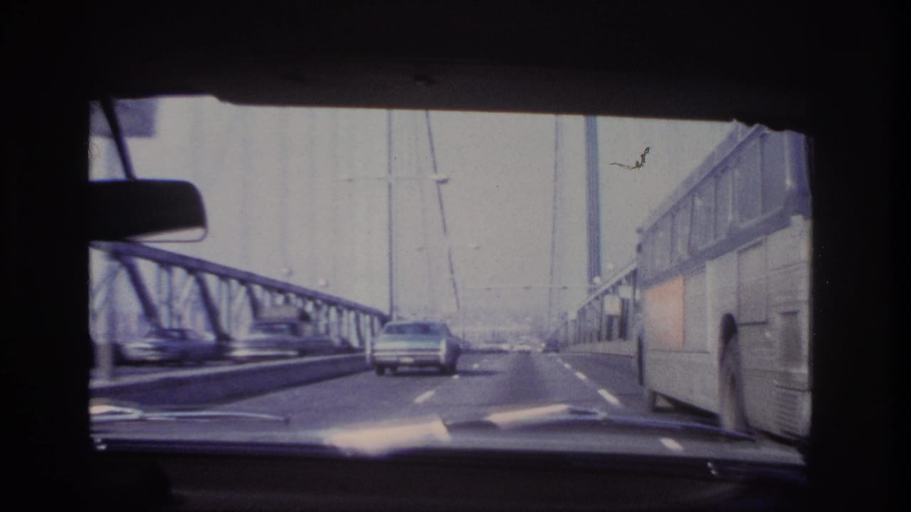 1966 home-movie frame from a moving car as a large coach bus passes on the right side of a steel bridge roadway.