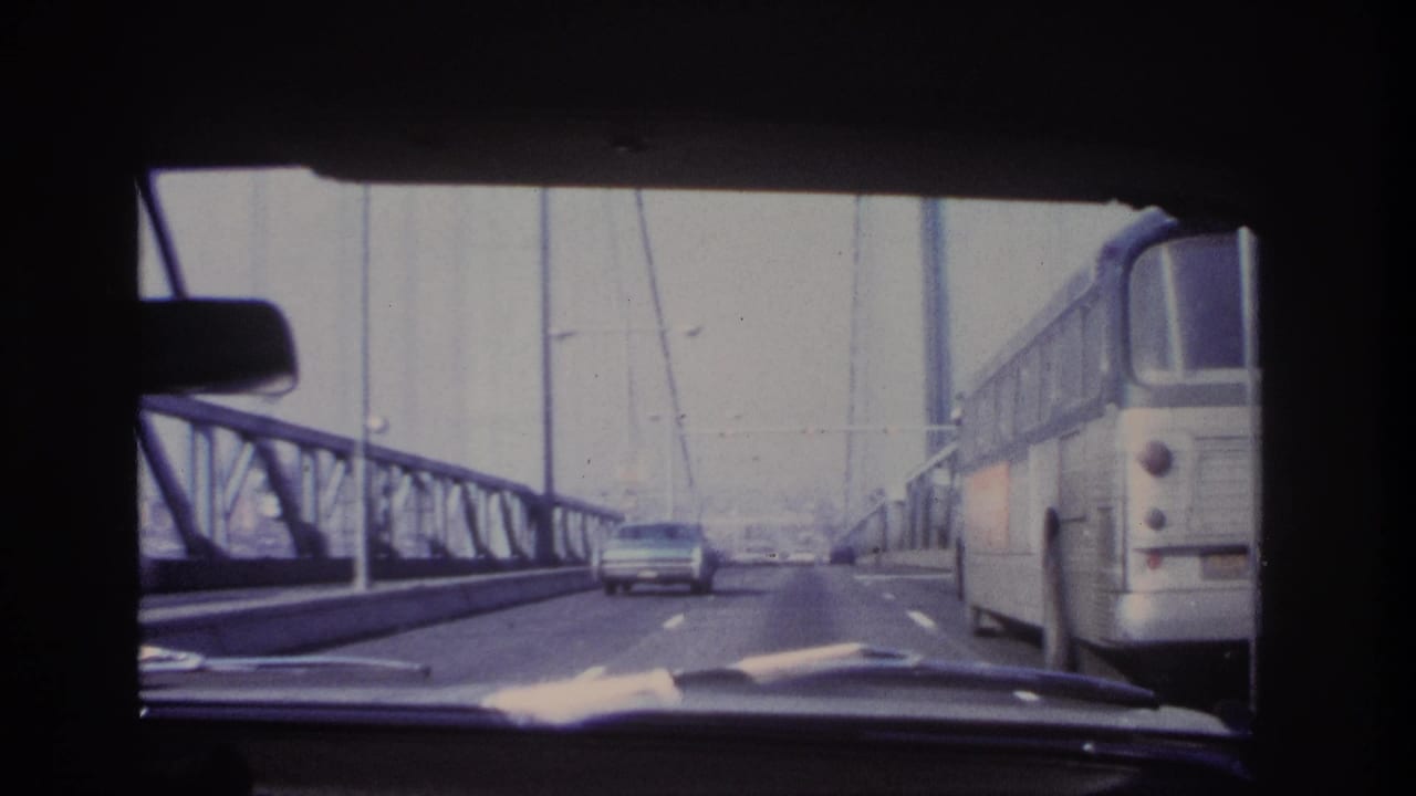Windshield view from a moving car on a steel bridge, with a large bus on the right and traffic ahead in the 1966 Hoboken metadata context.