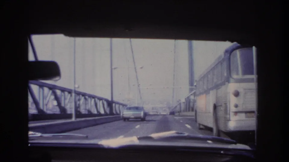 Windshield view from a moving car on a steel bridge, with a large bus on the right and traffic ahead in the 1966 Hoboken metadata context.