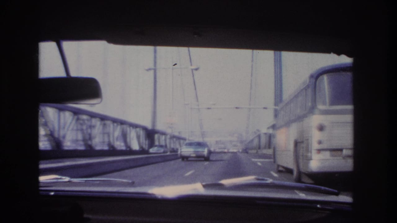 1966 Hoboken-area bridge crossing seen from inside a car, with a bus to the right, a sedan ahead, steel railings, and suspension cables.