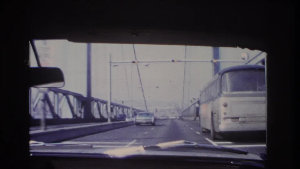 Windshield view on a Hoboken, New Jersey bridge in 1966, showing a bus along the right lane, a sedan ahead, and steel bridge structure.