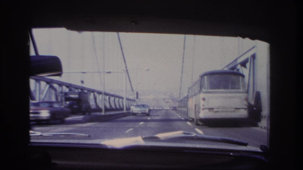 Late frame of the 1966 Hoboken bridge crossing, with a bus at right, a car ahead, passing traffic at left, and steel bridge railings.