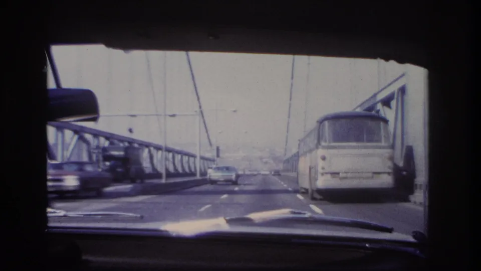 Late frame of the 1966 Hoboken bridge crossing, with a bus at right, a car ahead, passing traffic at left, and steel bridge railings.