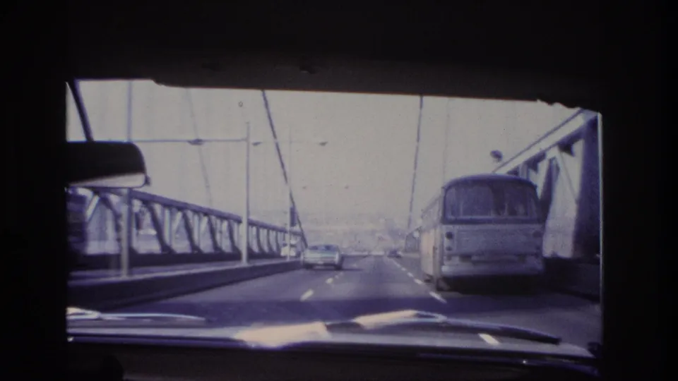 1966 Hoboken-area 8mm view through a car windshield as traffic and a bus travel across a steel bridge.