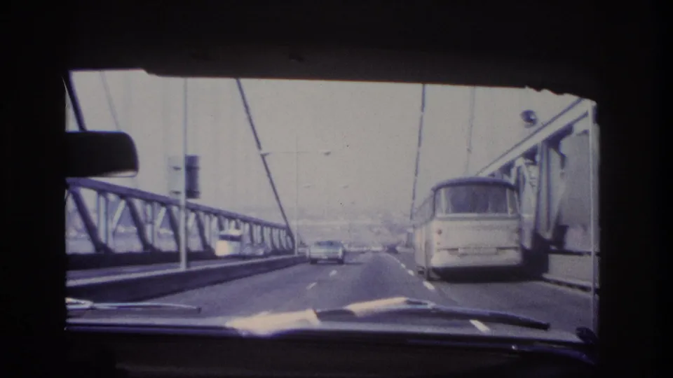 Car-interior view of 1966 bridge traffic near Hoboken, with a bus to the right and cars ahead on the roadway.