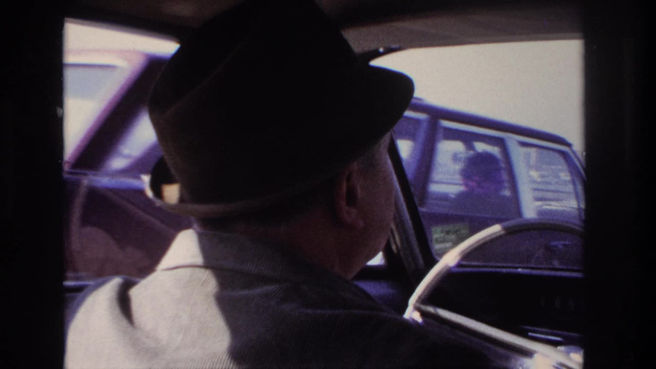 1966 Hoboken-area car interior view with a fedora-wearing driver and a nearby automobile visible through the side window.
