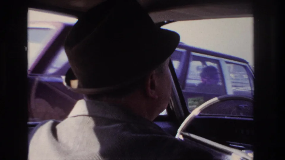 1966 Hoboken-area car interior view with a fedora-wearing driver and a nearby automobile visible through the side window.