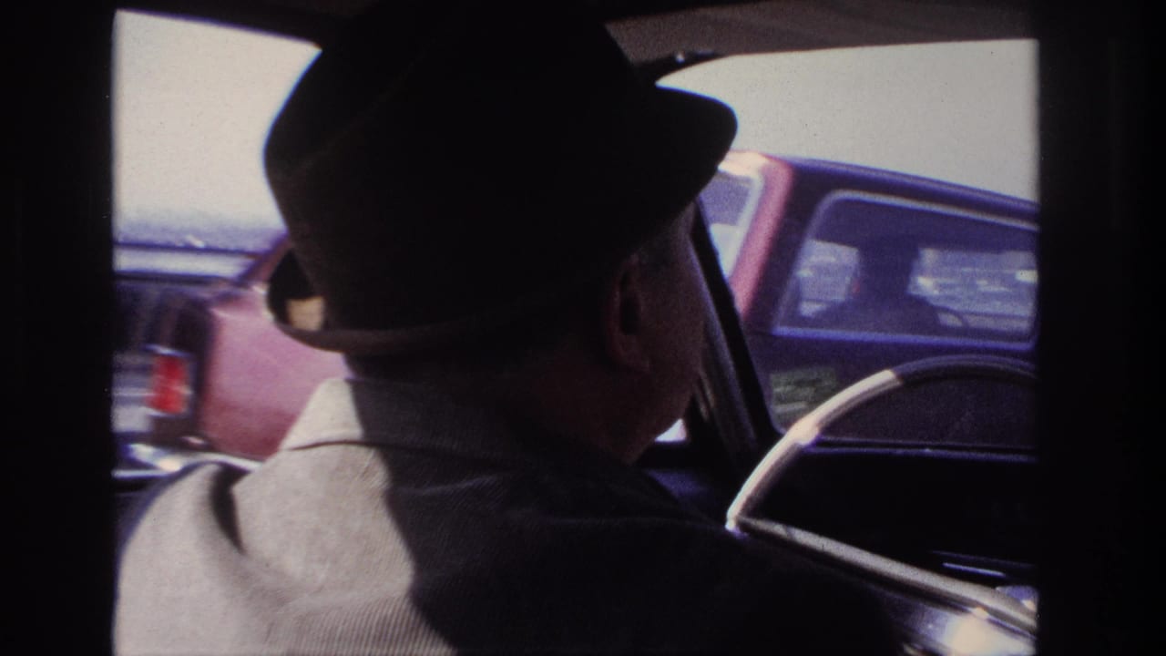 1966 Hoboken-area home movie frame showing an older man in a fedora driving, with passing cars visible through the window.