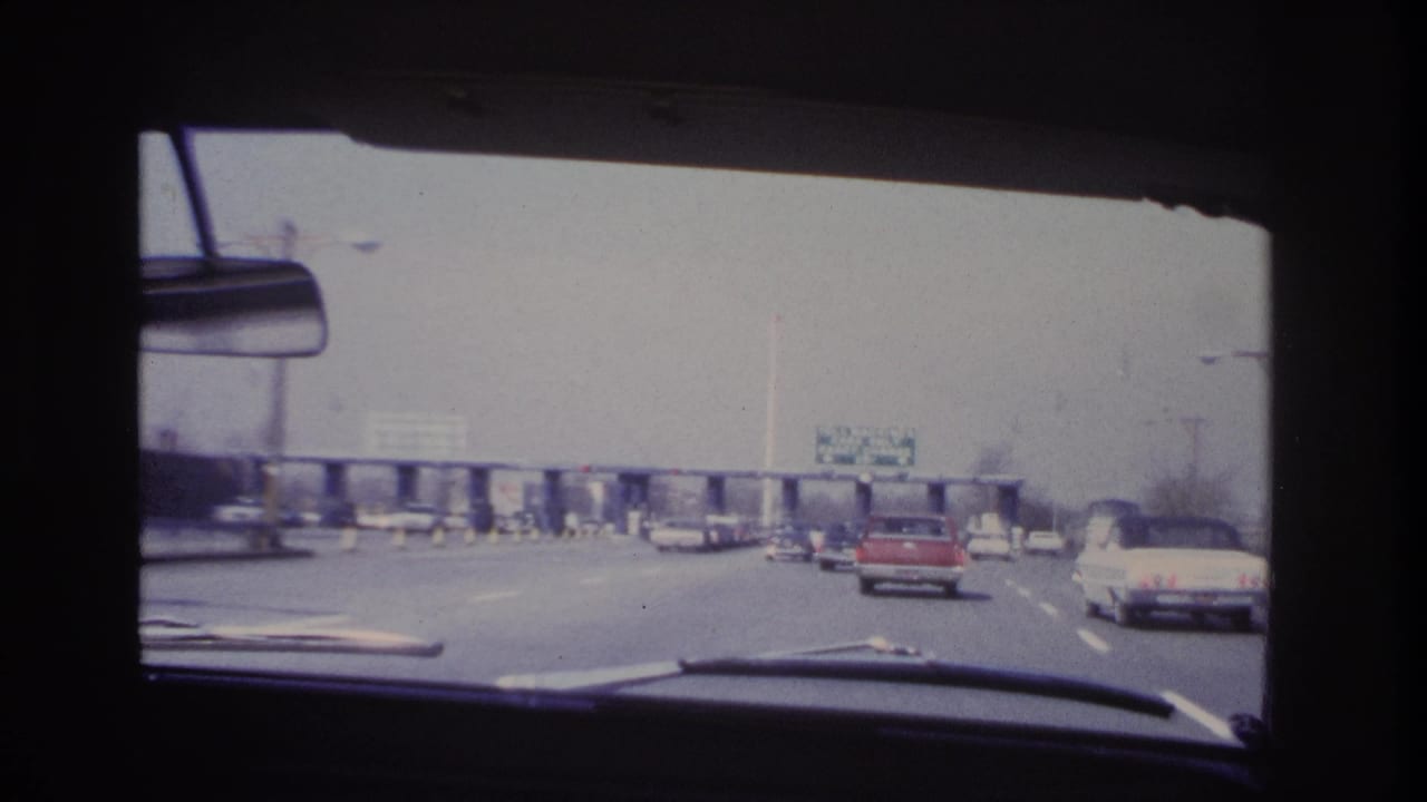 1966 Hoboken-area windshield view of 1960s cars approaching a toll plaza, with overhead signage and a red car ahead.