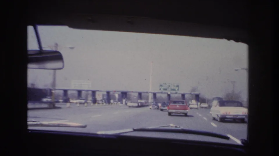 1966 Hoboken-area windshield view of 1960s cars approaching a toll plaza, with overhead signage and a red car ahead.