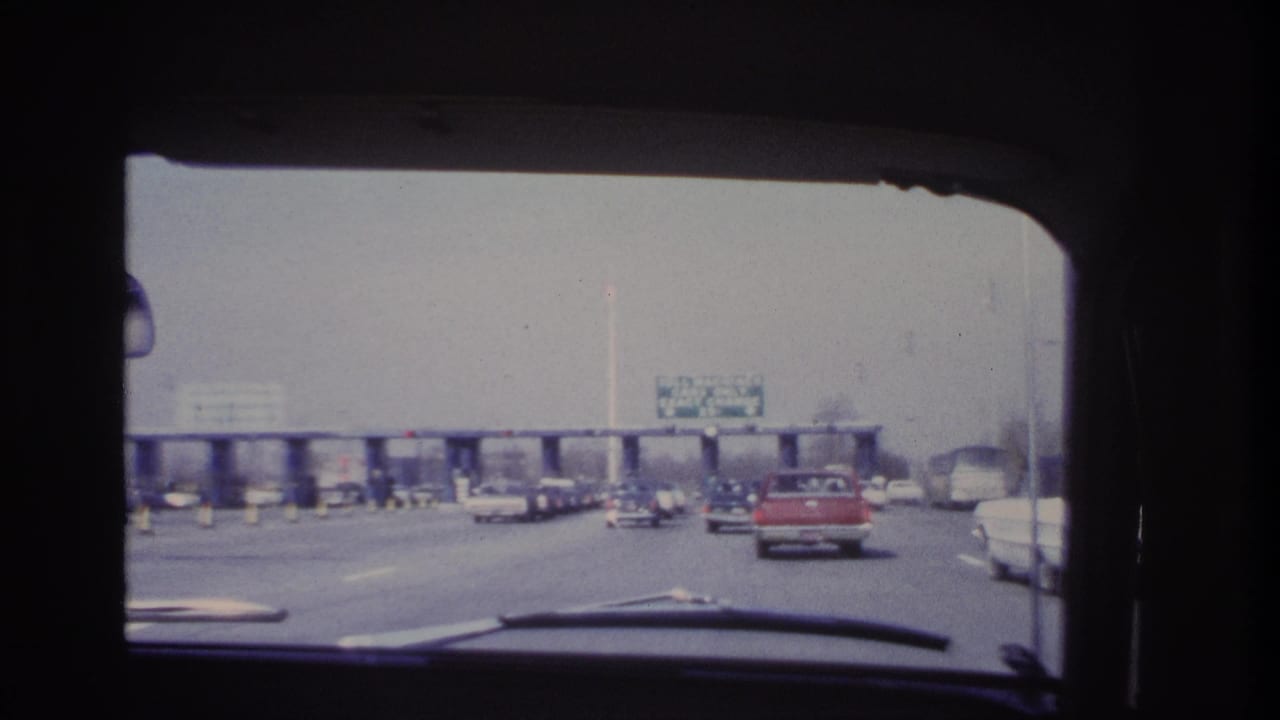 Windshield view from 1966 Hoboken-area home-movie footage showing classic cars closing in on a toll plaza.