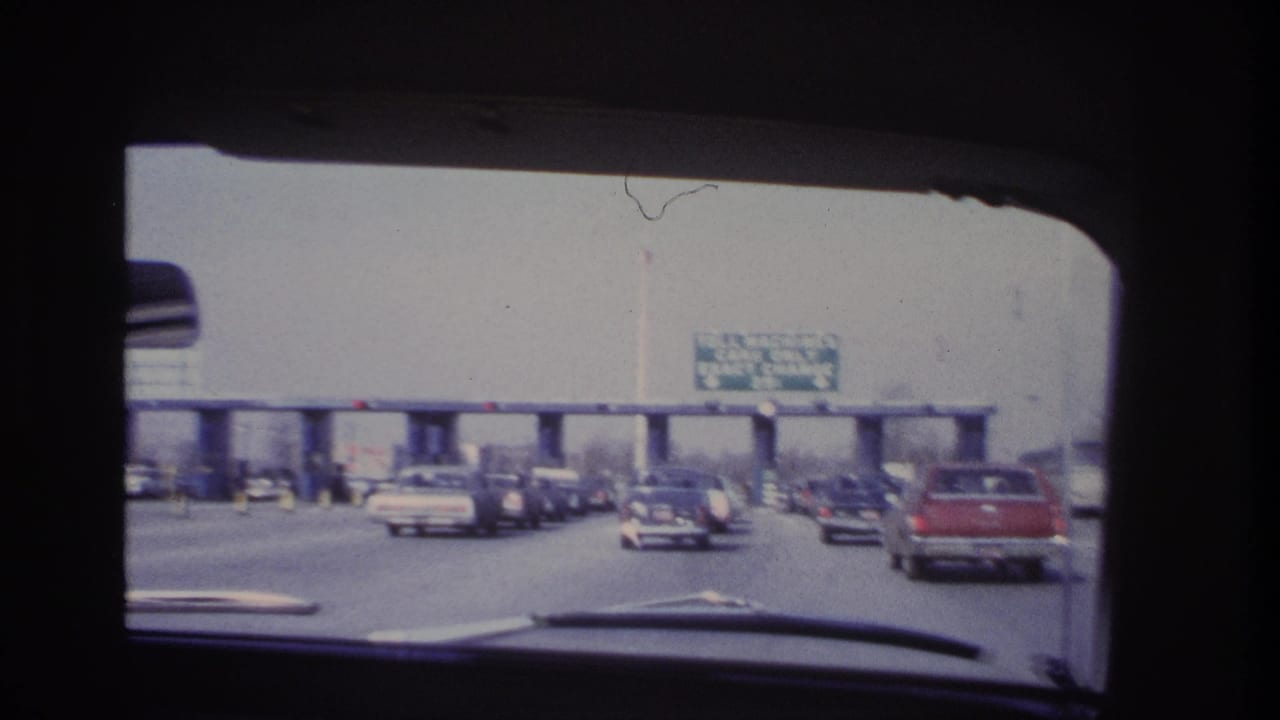 1966 Hoboken-area home-movie view through a car windshield toward toll booths, traffic, and an overhead exact-change sign.