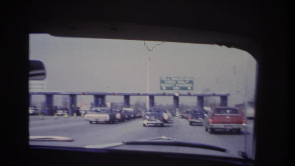 1966 Hoboken-area home-movie view through a car windshield toward toll booths, traffic, and an overhead exact-change sign.