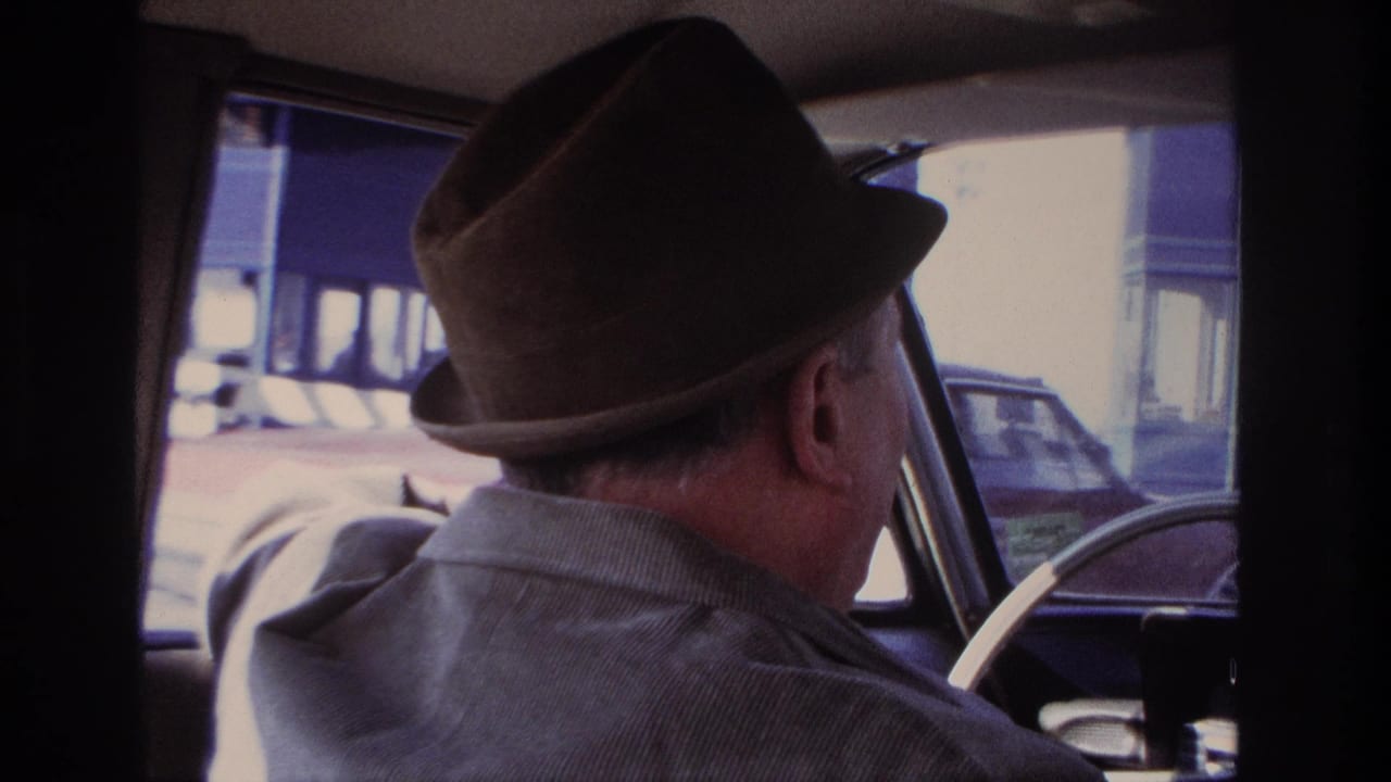 The 1966 Hoboken home movie shows the driver's profile, fedora, shoulder, steering wheel, and passing cars through the windshield.