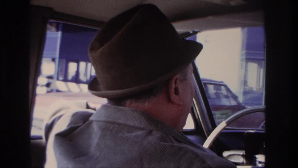 The 1966 Hoboken home movie shows the driver's profile, fedora, shoulder, steering wheel, and passing cars through the windshield.