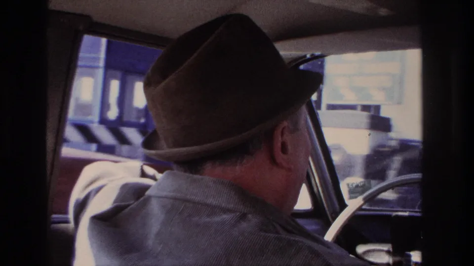 From the rear seat, the home movie records the older driver and bright, blurred Hoboken streetfronts outside the car window.