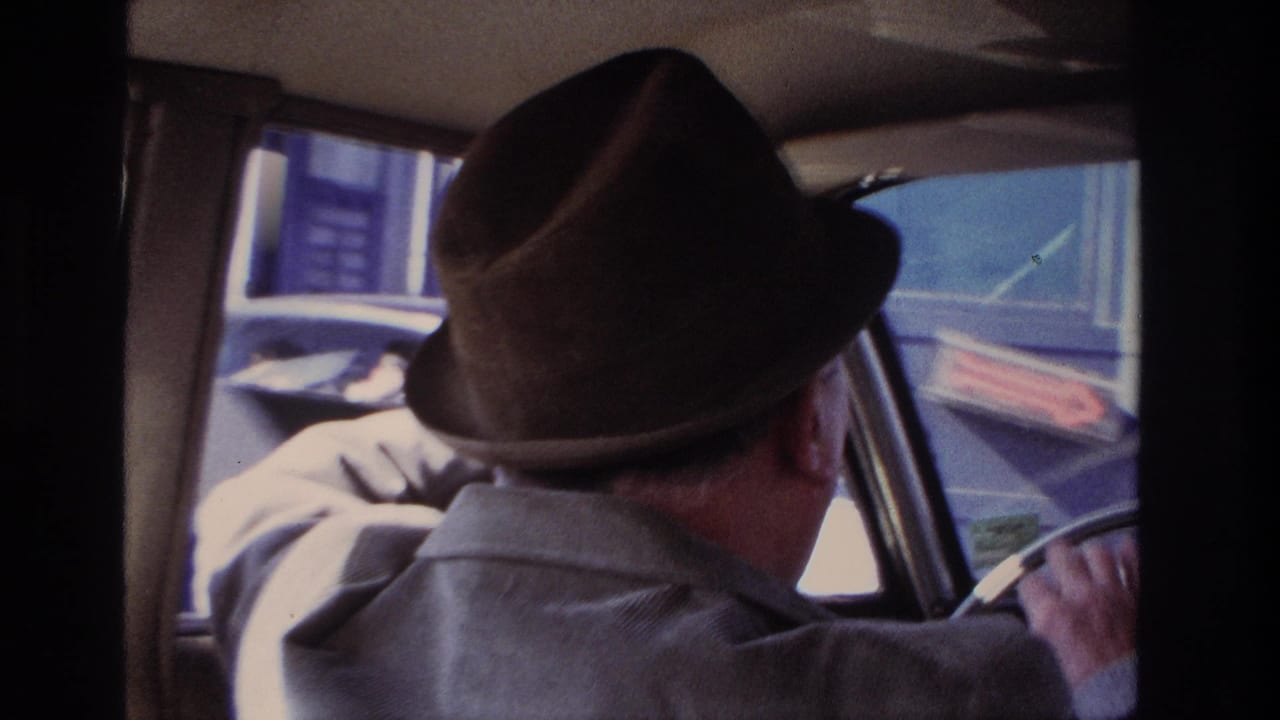 The clip ends with the older driver turning slightly at the wheel as Hoboken street scenery passes outside the car windows.