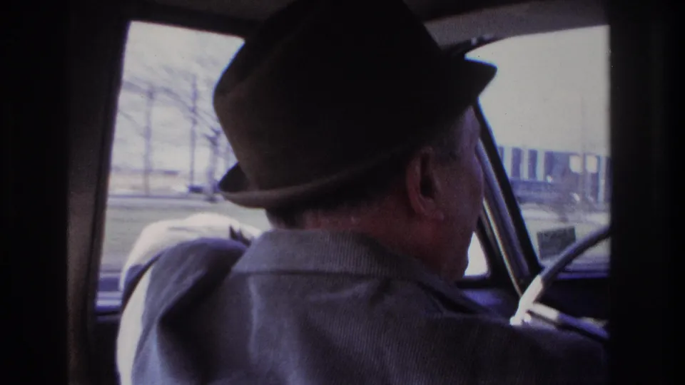 In 1966 Hoboken home-movie footage, a man in a dark fedora is filmed from behind while driving past roadside buildings.