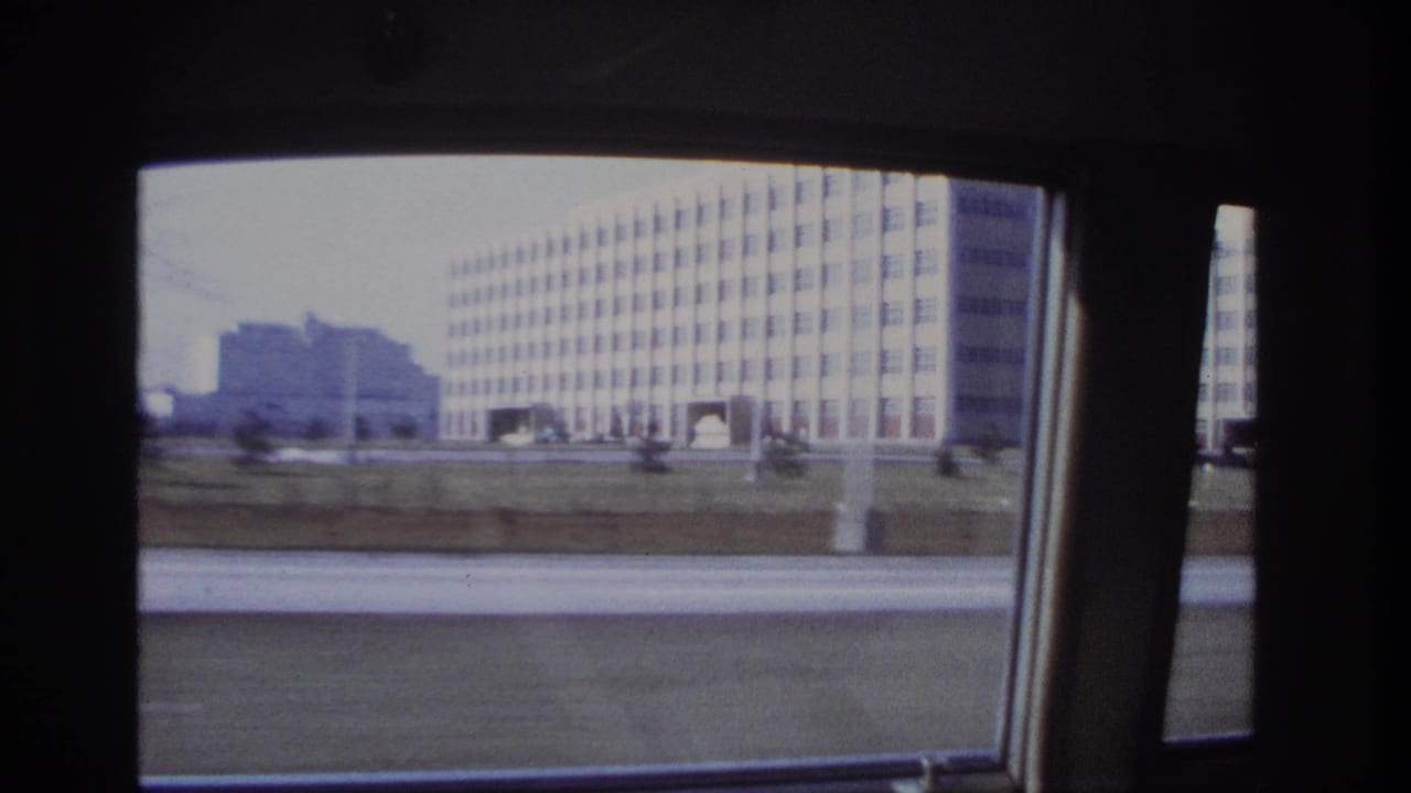 1966 Hoboken roadside view through a car window, centered on a large grid-window building with grass and pavement in the foreground.