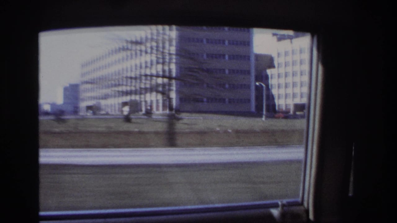End of a 1966 Hoboken car-window shot, with large roadside buildings, grass, pavement, and dark interior window framing.