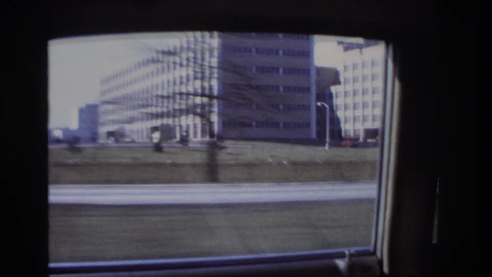 End of a 1966 Hoboken car-window shot, with large roadside buildings, grass, pavement, and dark interior window framing.