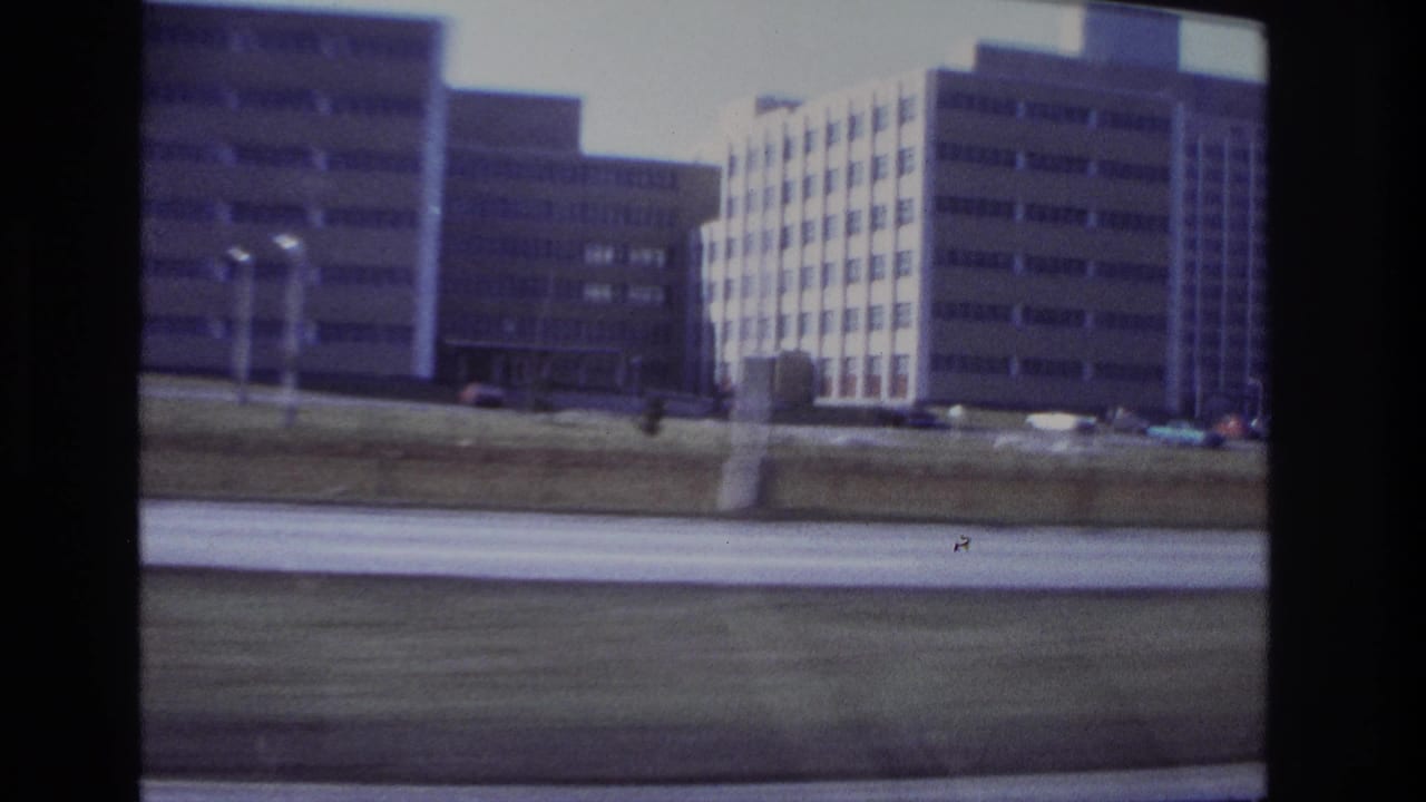 Large rectangular buildings and a road seen from a moving vehicle.