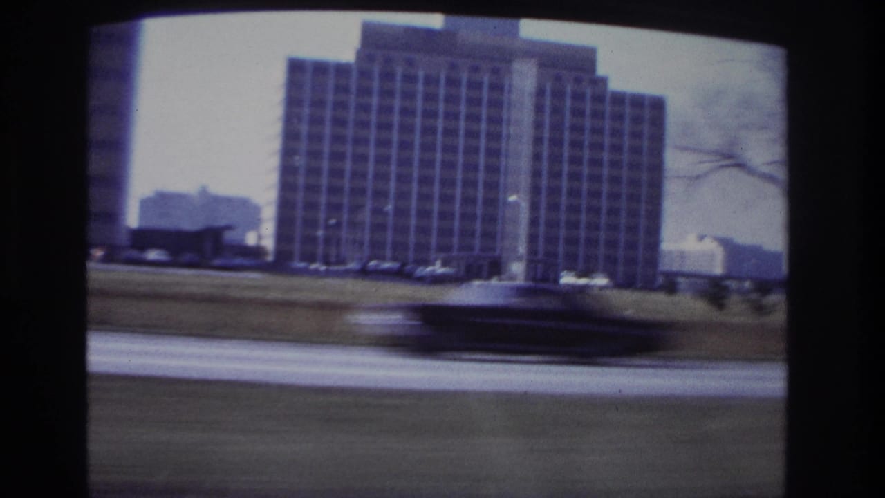 1966 Hoboken car-window view of a large gridded building with a blurred passing car in the foreground.