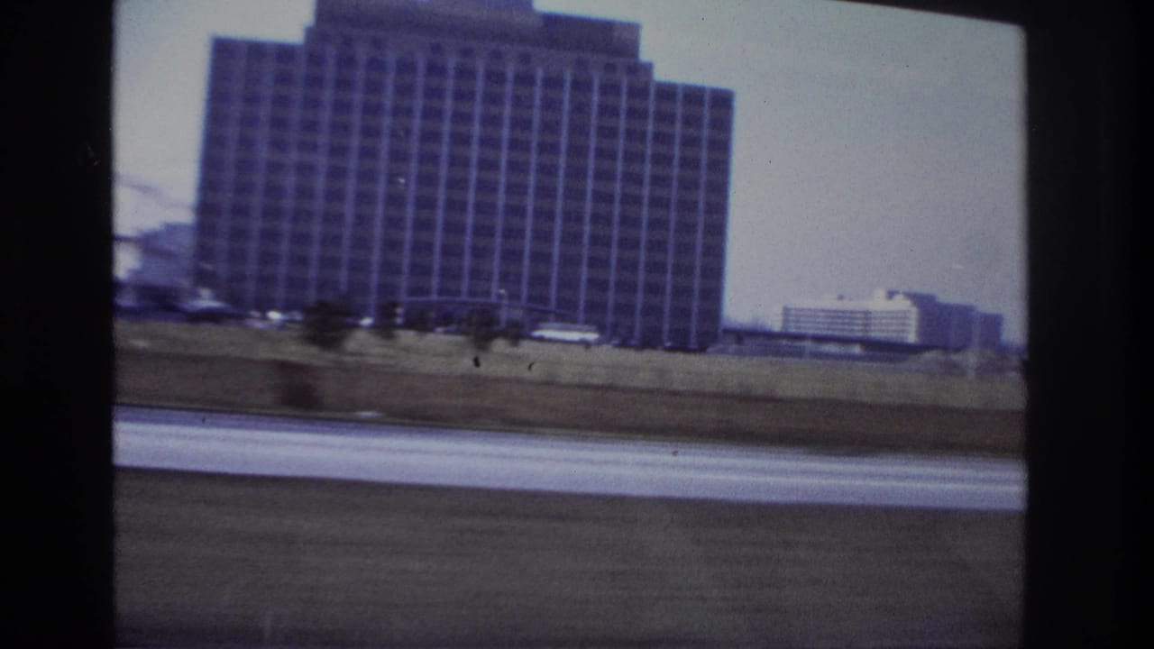 Roadside view of a large office-like building and passing traffic.