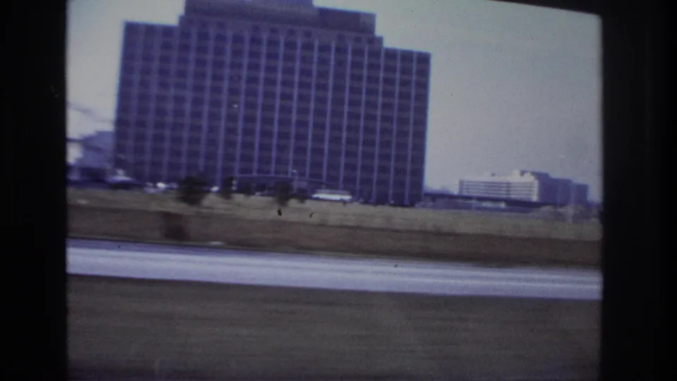 1966 Hoboken roadside view from a moving car, centered on a tall gridded building with traffic blur below.
