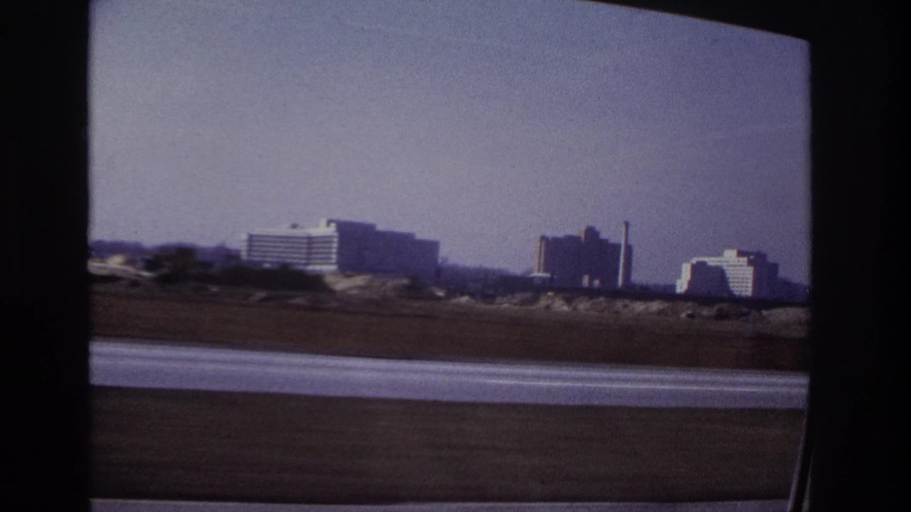 1966 Hoboken highway view from inside a moving car, with distant modern buildings under a hazy sky.