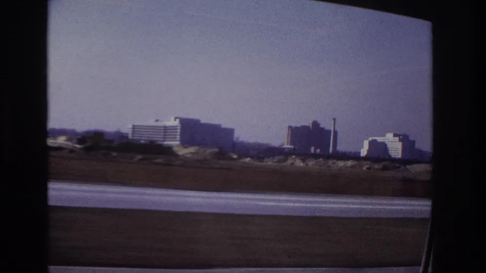 1966 Hoboken highway view from inside a moving car, with distant modern buildings under a hazy sky.