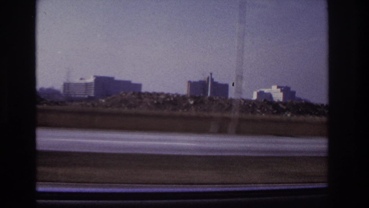 End-frame highway view near Hoboken, with distant modern buildings, a smokestack, and soft 8mm motion blur.