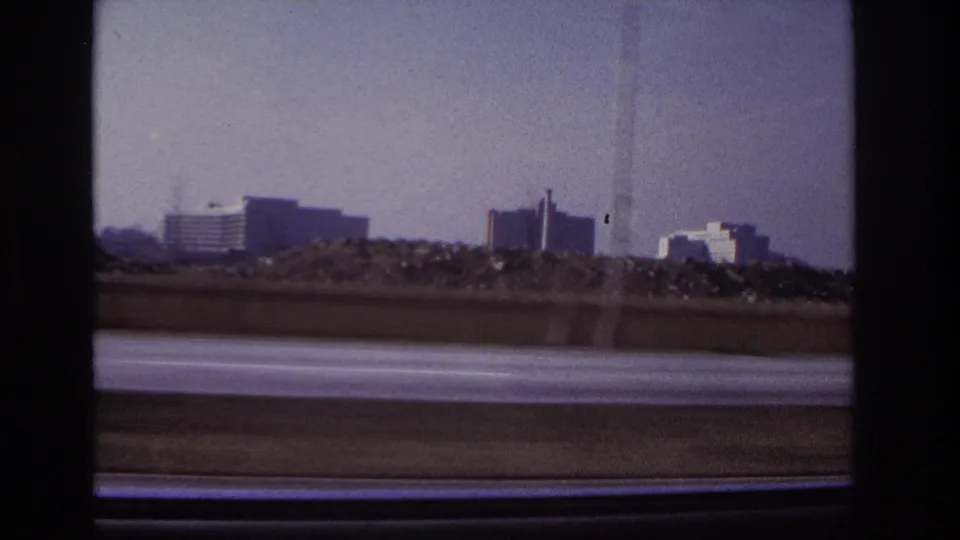 End-frame highway view near Hoboken, with distant modern buildings, a smokestack, and soft 8mm motion blur.