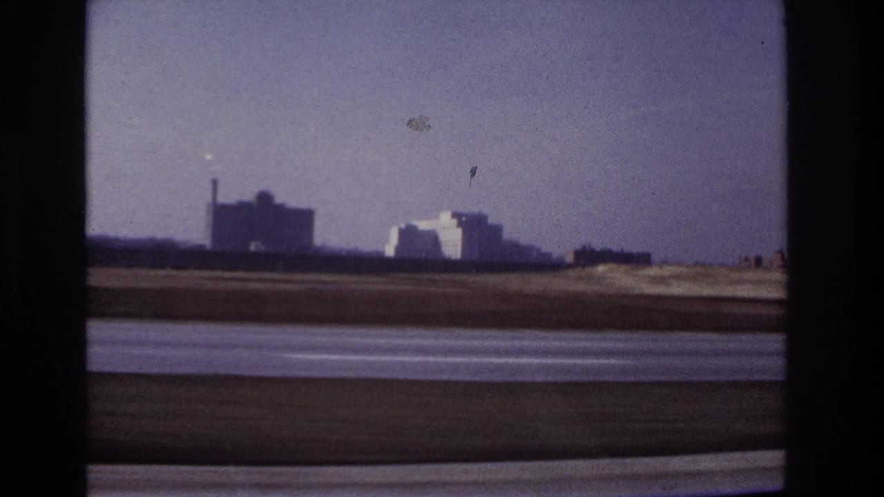 Roadside landscape with distant industrial buildings seen through a car window.