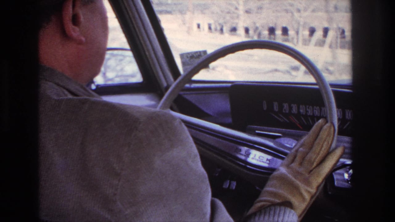 Inside a 1966 Hoboken-area driving shot, the driver’s gloved hand reaches near the older car dashboard and analog speedometer.