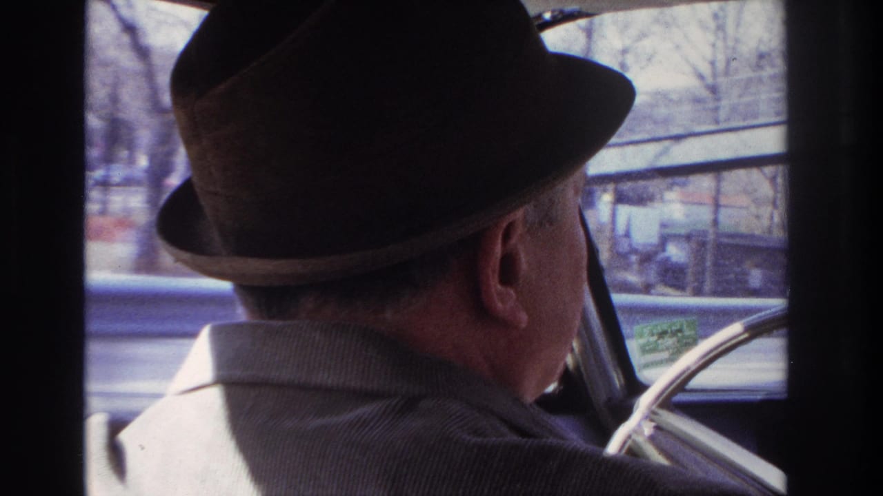 1966 Hoboken-area home-movie frame showing a man in a dark fedora and corduroy jacket driving, with bare trees outside the window.