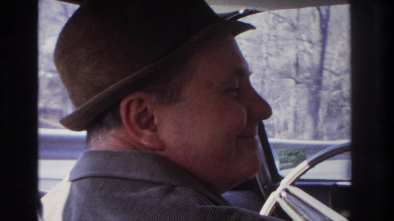 1966 home-movie frame showing an adult man in a brown fedora and corduroy jacket smiling from inside a car in New Jersey metadata context.