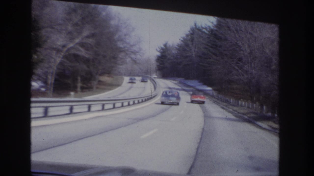 Two cars drive ahead on a divided road with snow along the right shoulder.