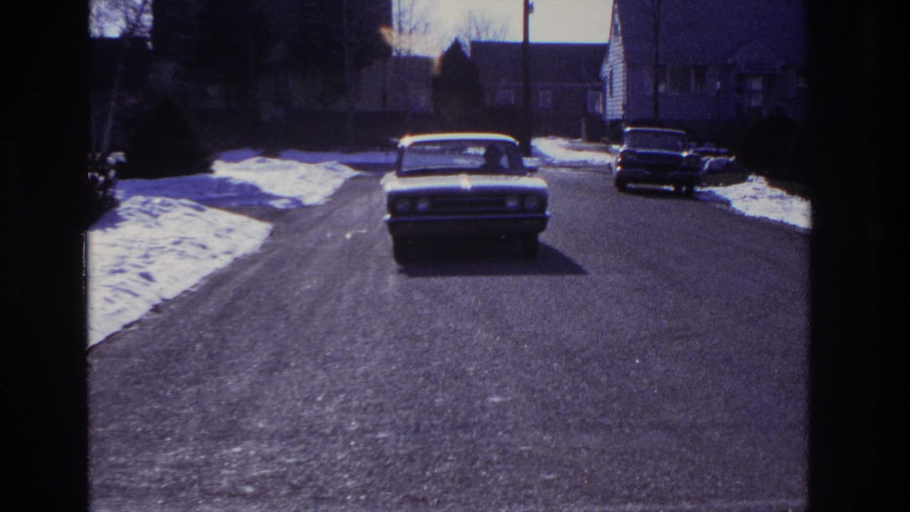 The classic sedan nears the fixed camera position on a snow-lined residential street in the 1966 Hoboken clip.