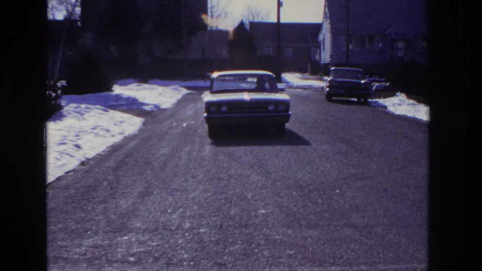 The classic sedan nears the fixed camera position on a snow-lined residential street in the 1966 Hoboken clip.