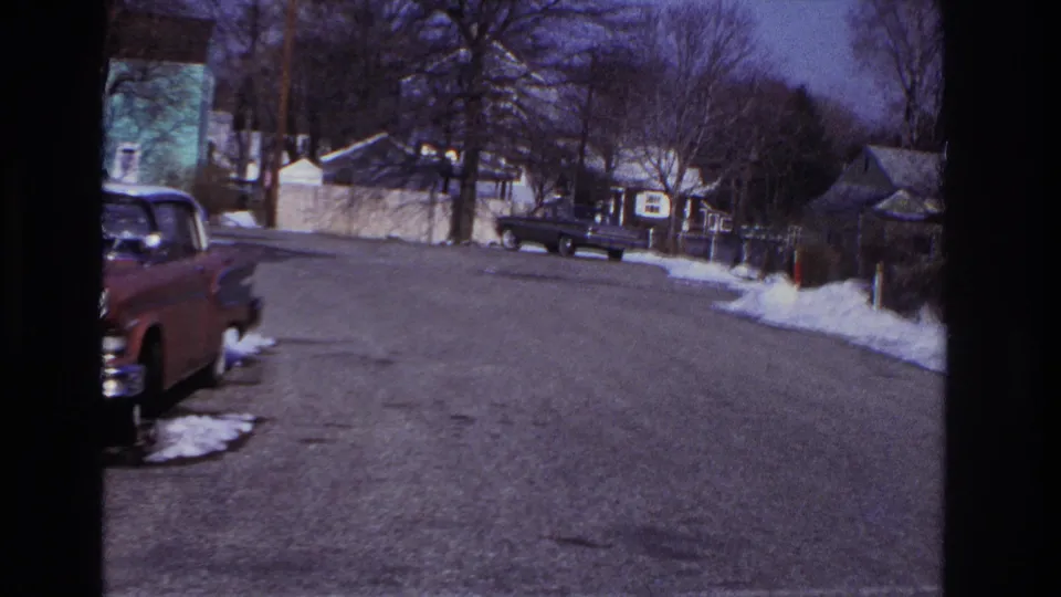 Snow-lined Hoboken residential street with parked mid-century cars, houses and bare winter trees in 1966 footage.