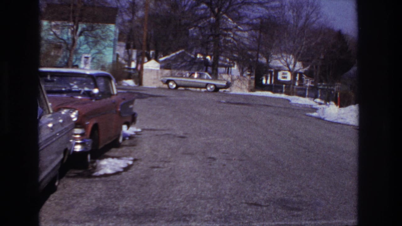 1966 Hoboken street view with parked mid-century cars along the curb, snow patches and modest houses in the background.