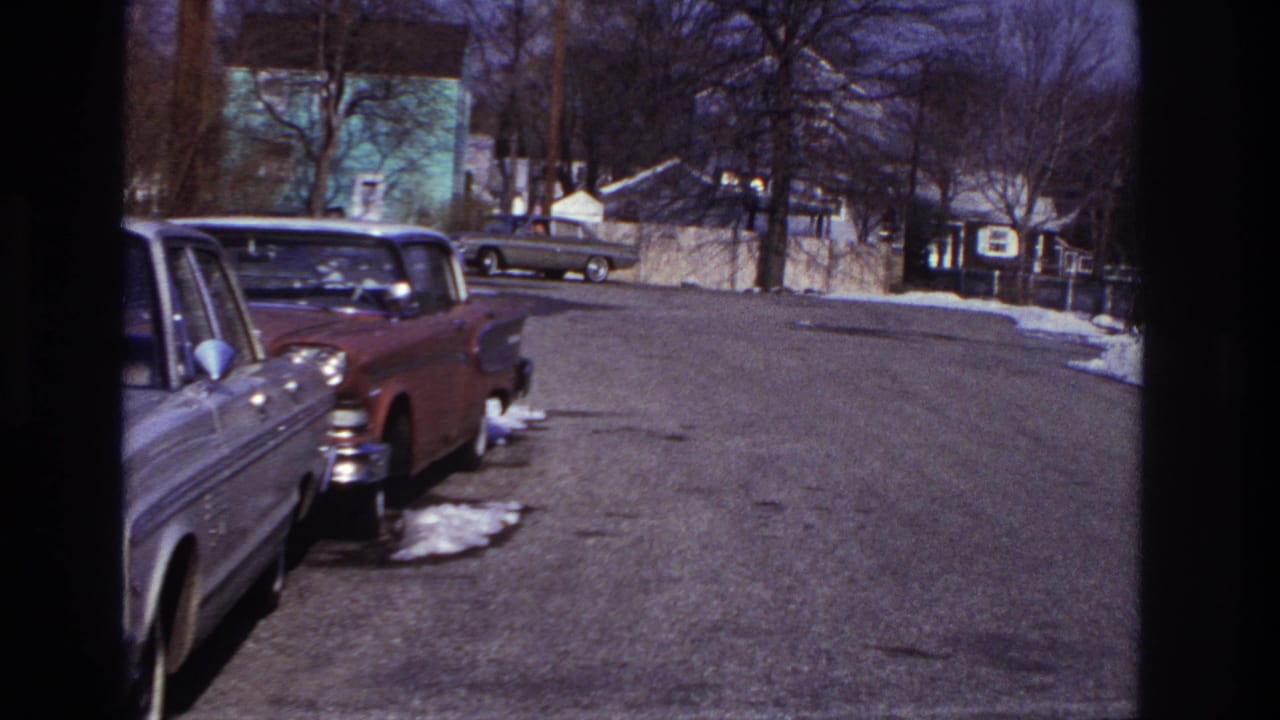 Hoboken 1966 home-movie frame showing parked cars, a broad residential street, snow patches and bare trees.