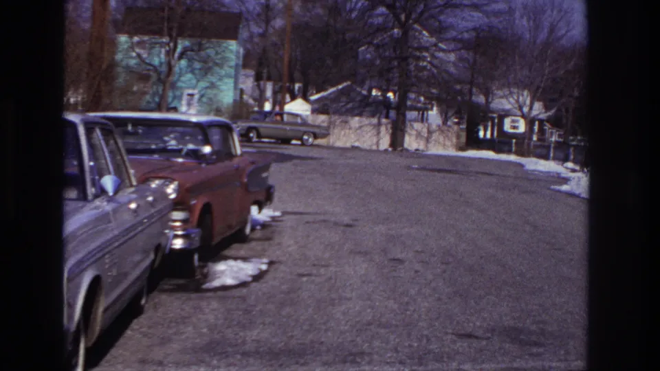 Hoboken 1966 home-movie frame showing parked cars, a broad residential street, snow patches and bare trees.