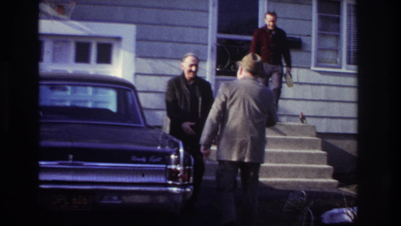 1966 Hoboken porch-side scene with adult men in coats near a parked car and house steps, suggesting a casual greeting or arrival.