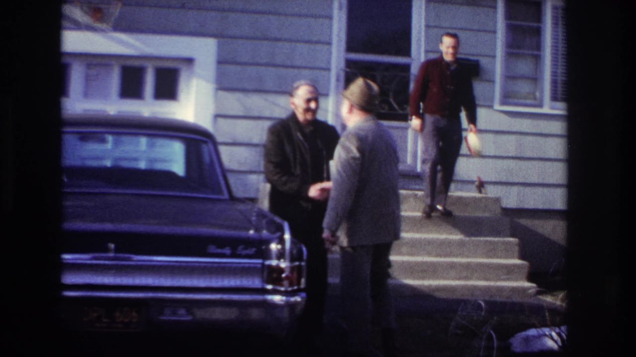 In supplied 1966 Hoboken footage, two adult men greet each other beside a dark sedan as another man stands on the front steps holding a hat.