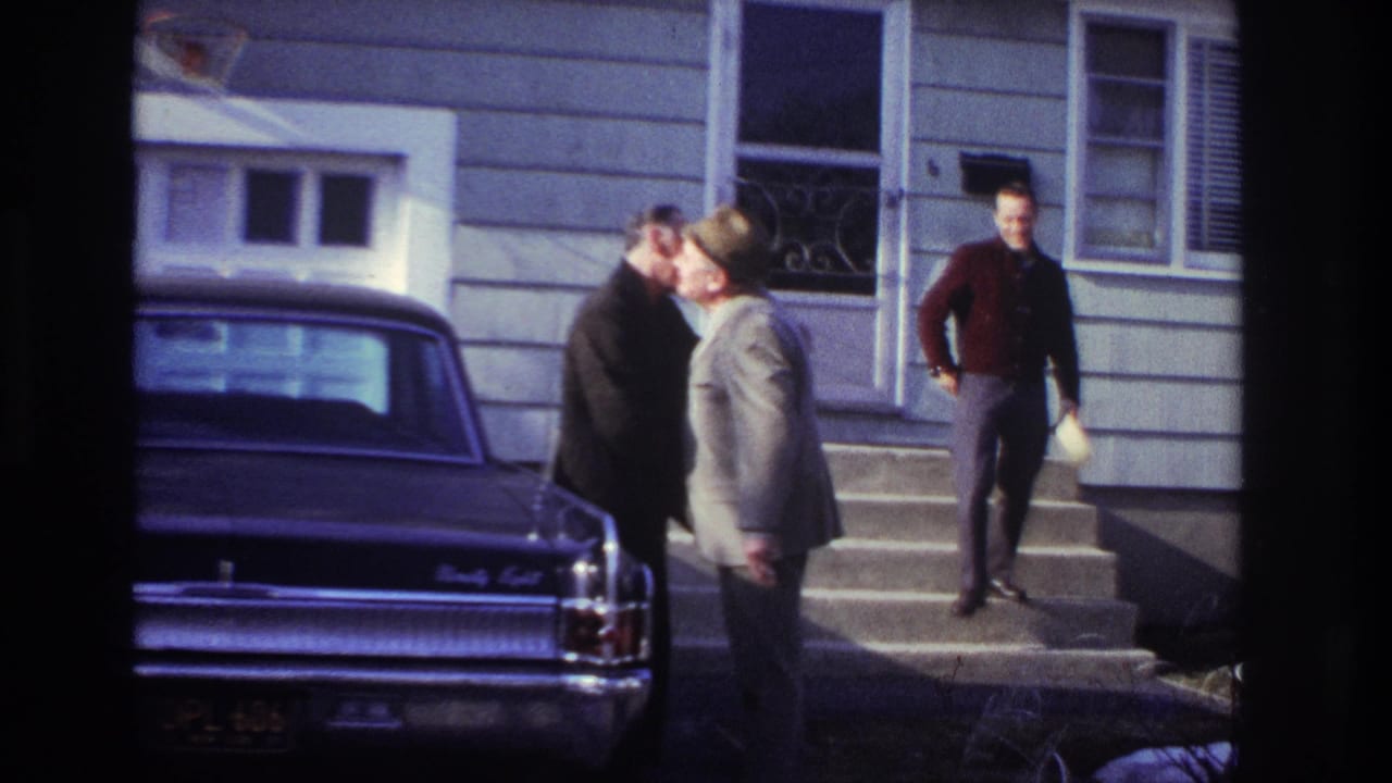 Two men stand close beside a sedan while another man walks down the steps holding a hat.